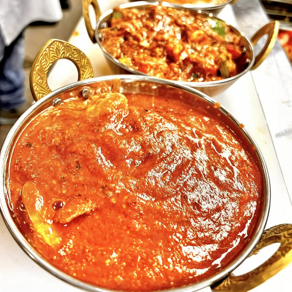 Two golden bowls of Kinara Indian Cuisine's vibrant orange curries, with one in sharp focus.