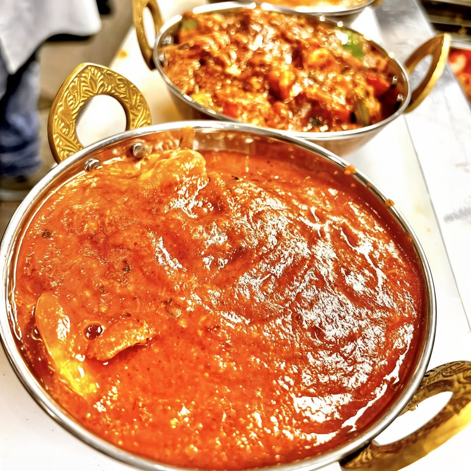 Two golden bowls of Kinara Indian Cuisine's vibrant orange curries, with one in sharp focus.
