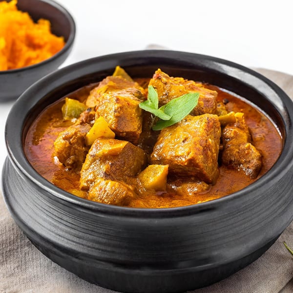 A black bowl of Kinara Indian Cuisine's rich, orange-brown curry with meat and potatoes, garnished with mint.