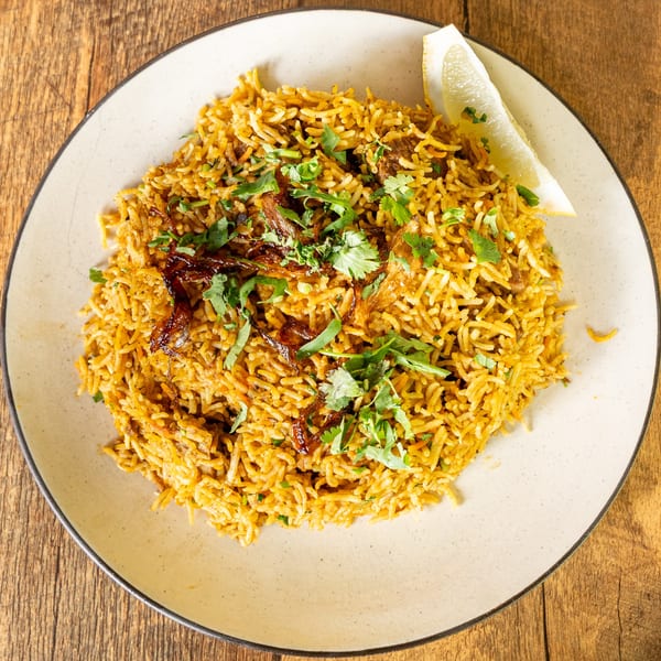 Kinara Indian Cuisine's biryani, garnished with fresh cilantro, crispy onions, and a lemon wedge.