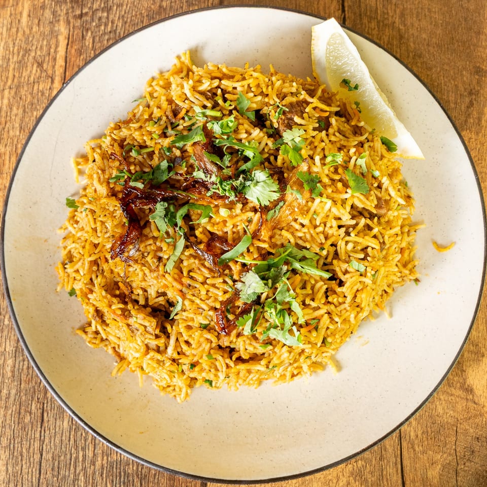 Kinara Indian Cuisine's biryani, garnished with fresh cilantro, crispy onions, and a lemon wedge.