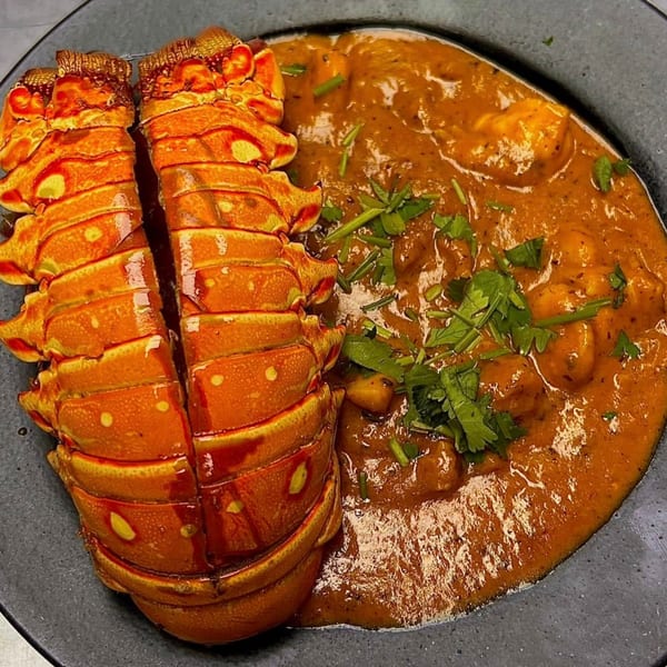 Split lobster tail and Indian curry with cilantro on a dark plate at Kinara Indian Cuisine.